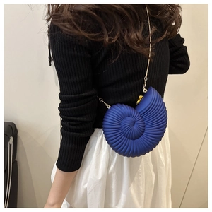 Detail of blue conch shell bag with gold chain strap on model with black sweater