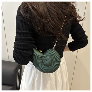 Detail of dark green conch shaped crossbody bag with gold chain on model's back