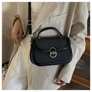 Detail view of black textured handbag with silver horseshoe clasp and woven flap