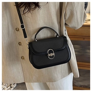 Detail of black crossbody bag with woven texture flap and silver U-shaped metal lock