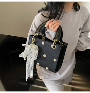Detail of black leather handbag featuring daisy embroidery and lace bow with pearls