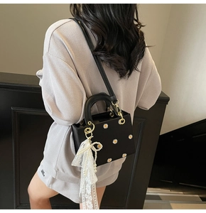 Close-up of black handbag with daisy embroidery, lace bow, and pearl charm detail