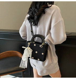 Detail of a black leather handbag featuring white daisy prints and pearl lace charm