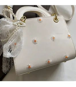 Close-up of white woven daisy bag featuring pearl charms and delicate lace bow details