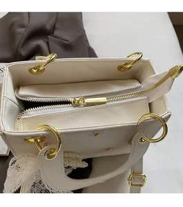 Detail of golden metal zipper and daisy embroidery on white lace handbag