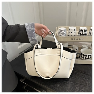 Detail of cream bucket bag featuring contrast black trim and dual handle design