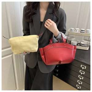 Detail of red leather tote bag with white stitching and yellow fabric pouch with zipper