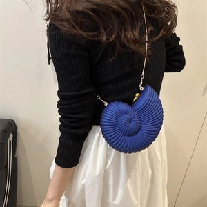 Deep blue conch-shaped crossbody bag with gold chain strap on female model