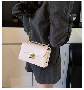 Detail of cream crossbody bag featuring a gold twist lock and metallic rivet studs