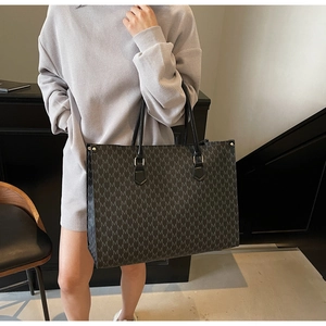 Close-up detail of large black tote bag featuring repeating M-pattern and sturdy handles