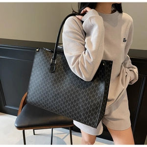 Detail view of a black tote bag with repeating M patterns on a grey casual outfit