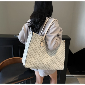 Detailed look at a large cream tote bag with M-pattern texture on a model's shoulder