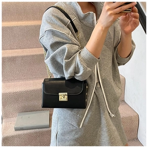 Detail of black leather square bag featuring a gold rotating lock and metal chain strap