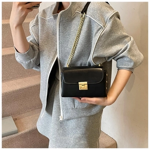 Detail of black leather square bag with gold chain strap and metal clasp on model