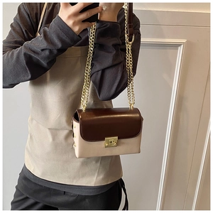 Detail of crossbody bag featuring brown flap contrast and gold chain shoulder strap