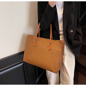 Detail of caramel tote bag with M-pattern print and leather handles in office setting