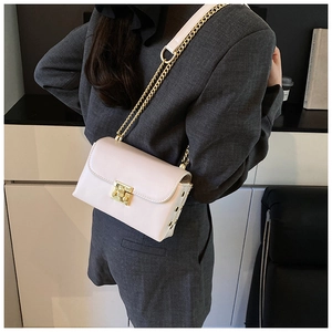 Detail shot of beige crossbody bag showing gold buckle and metal chain strap on model