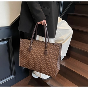 Detail view of brown tote bag with repeating M patterns held against a modern staircase