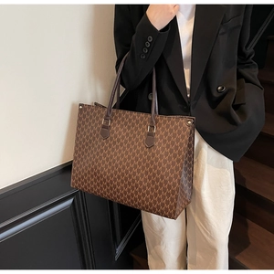 Detail shot of a large brown tote bag with vintage M-pattern print and dark leather handles