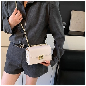 Detail of cream crossbody bag with gold lock and chain strap on a grey suit model