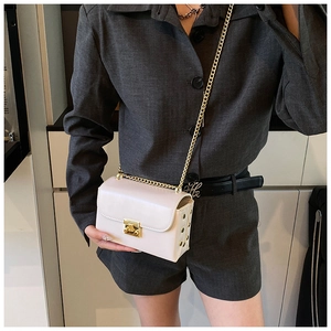Detail of white leather crossbody bag with gold chain strap and metallic buckle closure