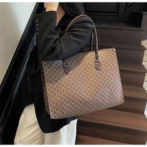 Detail of classic brown tote bag with M-letter monogram pattern and leather handle