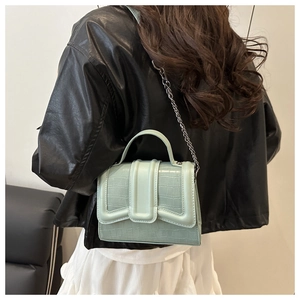 Detail of mint green crocodile pattern handbag with metal chain and top handle on model