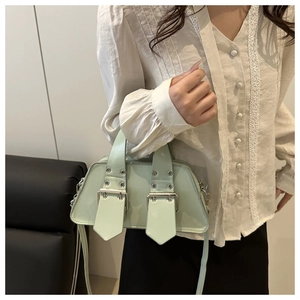 Detail view of mint green patent leather crossbody bag with silver buckles worn by a model