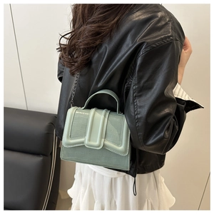 Detail of mint green crocodile pattern handbag with chain strap shown on model shoulder