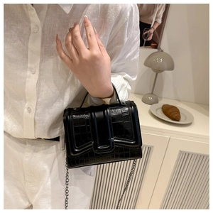Detail of black faux leather handbag with crocodile pattern on white shirt background