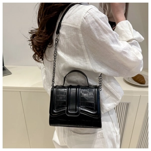Detailed view of black crocodile pattern handbag with metal chain strap worn by model