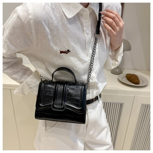 Close-up of model wearing a black crocodile pattern crossbody bag with chain strap