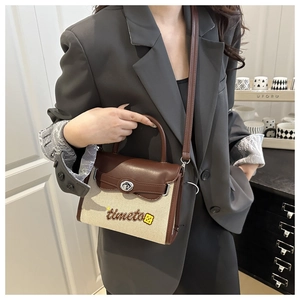 Detail of canvas and brown leather crossbody bag featuring metal turn-lock and embroidery