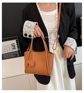 Brown leather bucket bag with elephant charm shown on a model in a black blazer