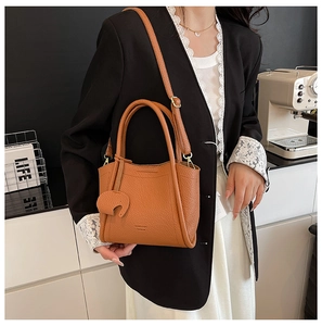 Detail of caramel leather bucket bag with elephant charm on model in black suit