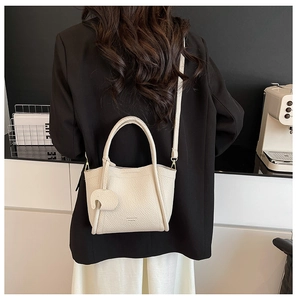 Minimalist beige pebble leather bucket bag shown on a model with heart charm and shoulder strap