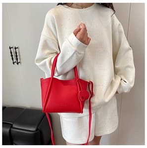 Detail of red lychee grain leather tote bag with heart charm and slim shoulder strap