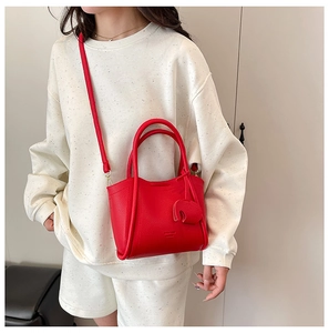Detail of red lychee grain leather tote with elephant charm and adjustable strap