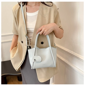 Detail of light blue bucket bag with leather texture, adjustable strap and elephant charm