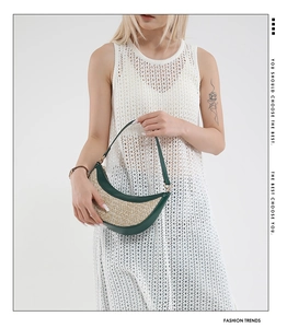 Detail of handwoven straw crescent bag with dark green leather piping and slim strap