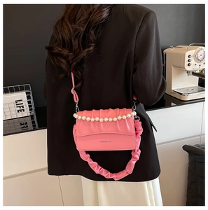 Detail of pink pleated crossbody bag with pearl chain strap worn over a black blazer