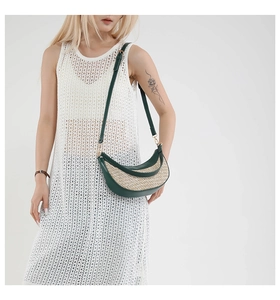 Detail of half-moon straw crossbody bag with green leather trim on a white lace dress