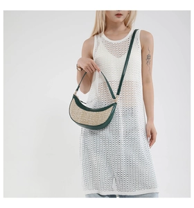 Detail of woven crescent bag with green leather trim and long shoulder strap on model