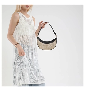 Detail of a crescent straw bag with black leather trim held by a model in a white dress