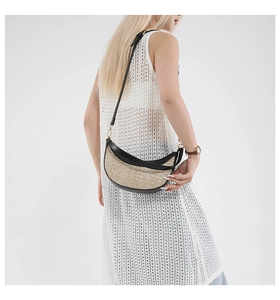 Detail view of woven straw crescent bag with black leather straps on a model