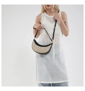 Detail of hand-woven straw crescent bag with black leather trim worn on the shoulder
