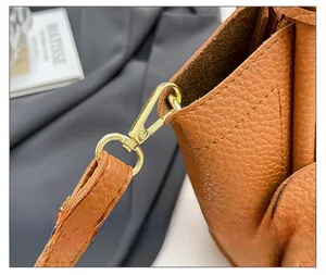 Detailed macro view of gold metal hooks and D-rings on brown lychee grain leather bag