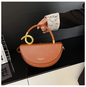 Detail of brown leather saddle bag featuring a round gold metal handle and twist accent