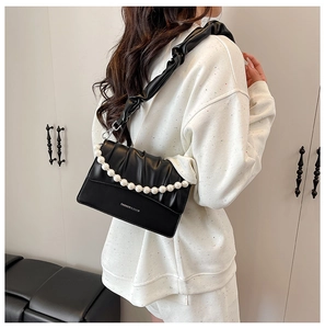 Close-up of black pleated crossbody bag with elegant white pearl chain detail and logo