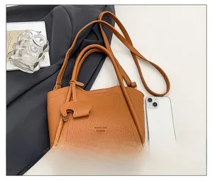 Detail view of caramel lychee grain leather tote with elephant charm and adjustable strap